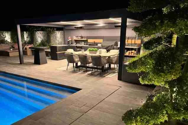Outdoor kitchen in Copthorne West Sussex with outdoor seating next to pool at night