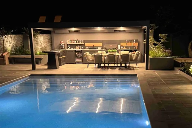 Outdoor kitchen in Copthorne West Sussex with outdoor seating next to pool at night