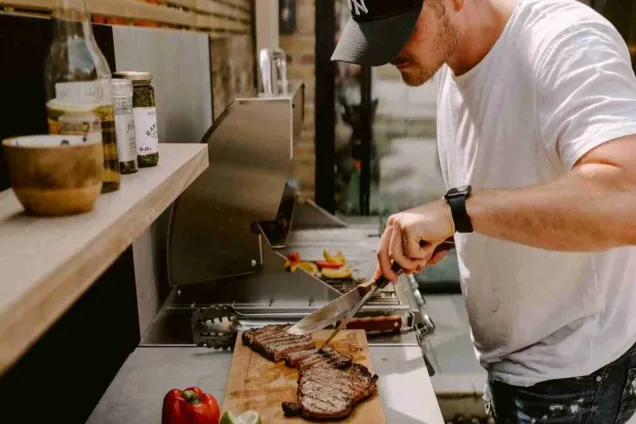 outdoor kitchen in chelsea london with man cutting steak on chopping board