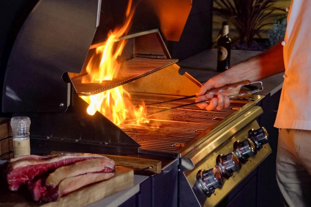 person cooking steak on bull gas grill with flames coming from grill