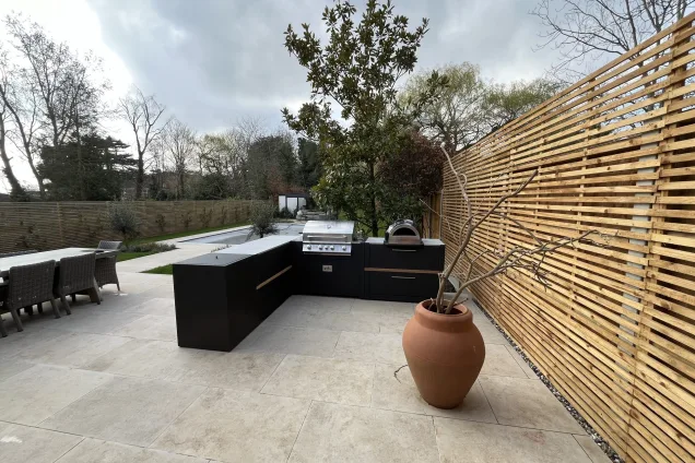 outdoor kitchen on with gas bbq and pizza oven patio with large decor pot, seating area, and pool view in Loughton garden