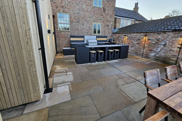 outdoor kitchen with bar seating on patio next to aged brick wall and wood cladding in Tockwith, York