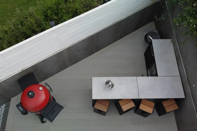 top-view of outdoor kitchen with bar seating, kamado-style BBQ and built-in fridge in patio corner in St Ives, Cornwall