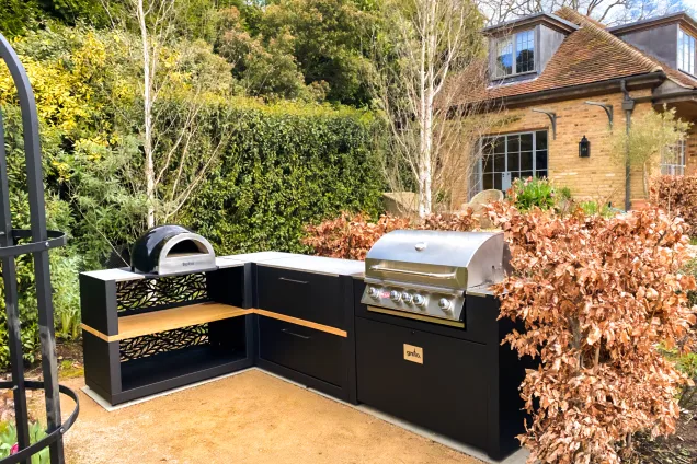 outdoor kitchen in established garden with bull gas grill station, storage cabinets and pizza oven