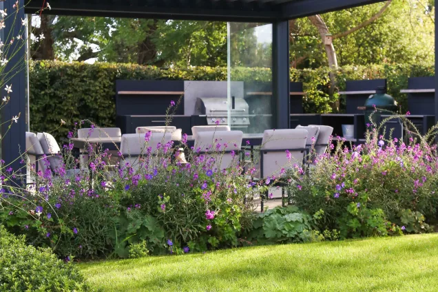 Dining area under pergola and flowerbed overlooking outdoor kitchen with Bull Gas Grill in Reigate