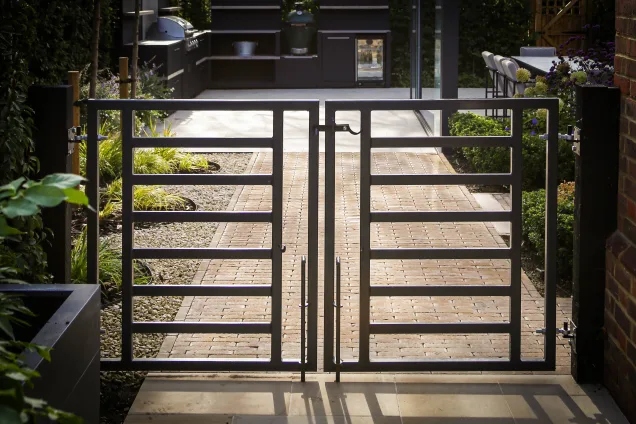 Metal garden gates overlooking outdoor kitchen in landscaped garden in Reigate