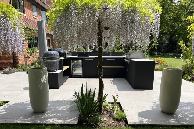 U-shaped outdoor kitchen with Gusto charcoal BBQ, pizza oven, built-in fridge, sink, and Bull gas grill on patio with wisteria tree in Reading, Berkshire