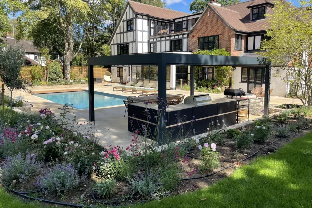 Outdoor kitchen in sussex under pergola next to outdoor pool and plants