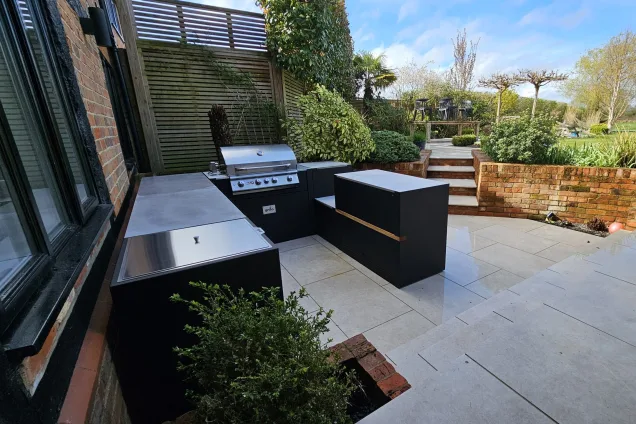 Outdoor kitchen in Berkshire with gas bbq and storage cabinet all on white patio with plants