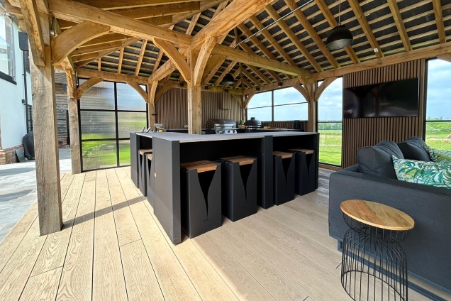 Outdoor kitchen in Hertfordshire with Bar table and stools and seating area and bull gas bbq under wooden cover