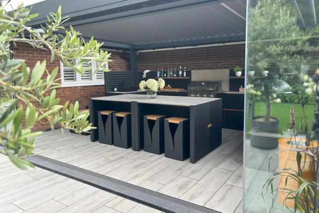 Outdoor kitchen in Hertfordshire under pergola with bar table and stools, gas bbq and worktop and storage space