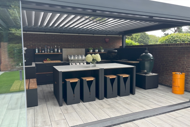 Outdoor kitchen in Hertfordshire under pergola with bar table and stools, gas bbq, charcoal bbq and worktop and storage space