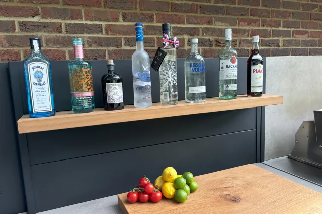 Outdoor kitchen in Hertfordshire with shelf cabinet with bottles on feature wall shelf