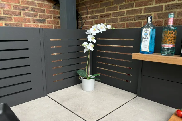 Outdoor kitchen in Hertfordshire with shelf cabinet with flower in corner of the slatted corner feature wall