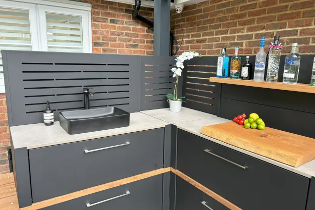 Outdoor kitchen in Hertfordshire with shelf cabinet with flower in corner of the slatted corner feature wall and built in sink
