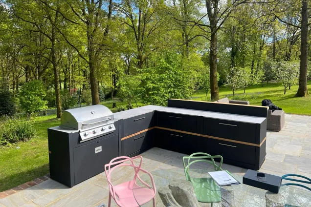 Outdoor kitchen in Cranleigh on patio in wooded garden with Bull gas bbq and bar cabinets and coloured chairs and table