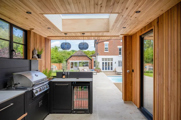 outdoor kitchen with drinks fridge and bin and bull gas grill station and outdoor pool in background