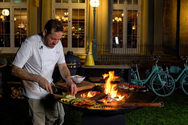 person cooking food on tall chefs anvil outside restaurant