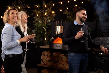 people socialising in grillo outdoor kitchen with pizza oven and gusto charcoal bbq