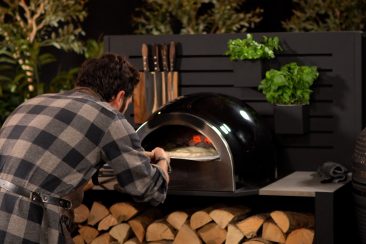 person putting calzone into wood fired pizza oven in grillo outdoor kitchen