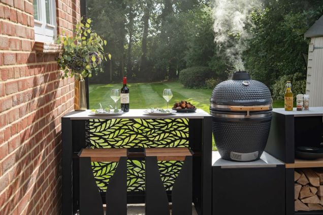 outdoor kitchen with bar table and stools and gusto charcoal bbq in large garden against a house