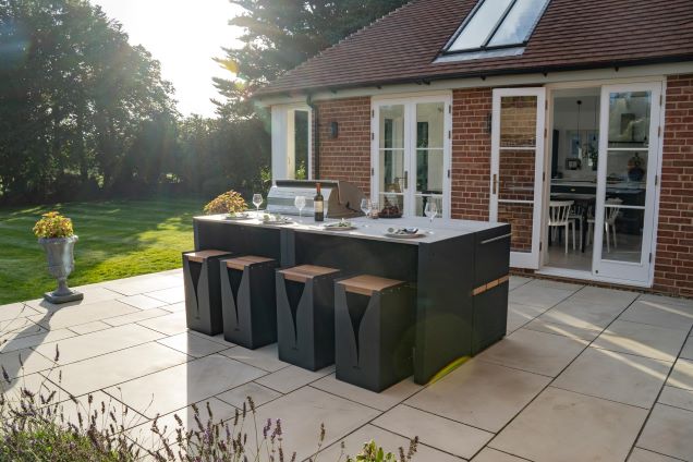 outdoor kitchen island layout on patio with bar table and stools and bbq