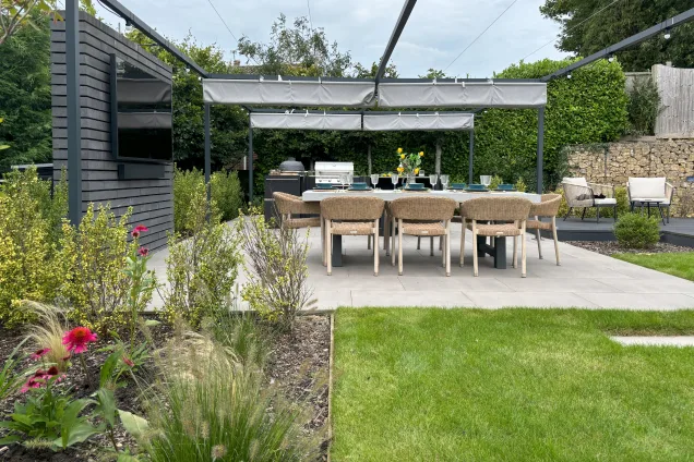 outdoor tv and dining table next to outdoor kitchen in garden