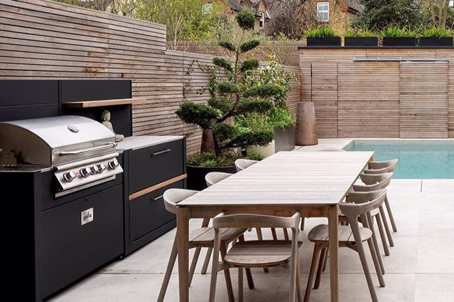 Grillo outdoor kitchen in a city garden, featuring Scandinavian-inspired dining furniture, a nearby pool, and lush potted plants creating a calm, contemporary outdoor space.