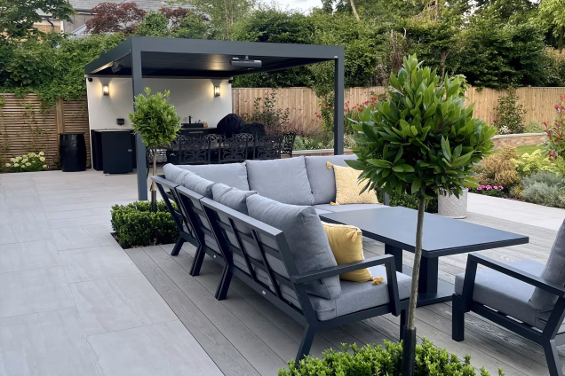 outdoor kitchen next to planters, under a pergola and on a large patio