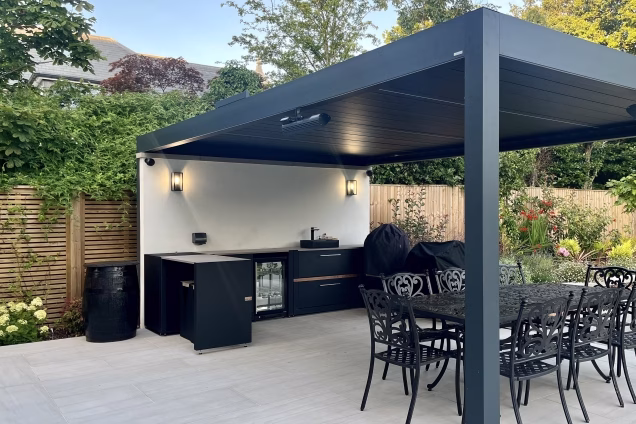 outdoor kitchen under grey pergola on light grey patio with sink and charcoal bbq