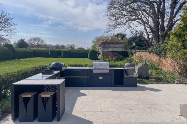 outdoor kitchen with bar table and stools, and a bull gas bbq, charcoal gusto bbq and pizza oven
