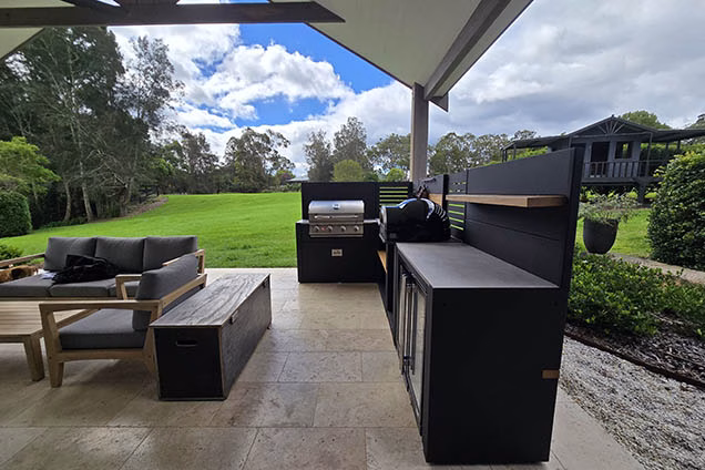 View looking out over a verdant grassy backyard framed by gum trees with an outdoor kitchen in the foreground