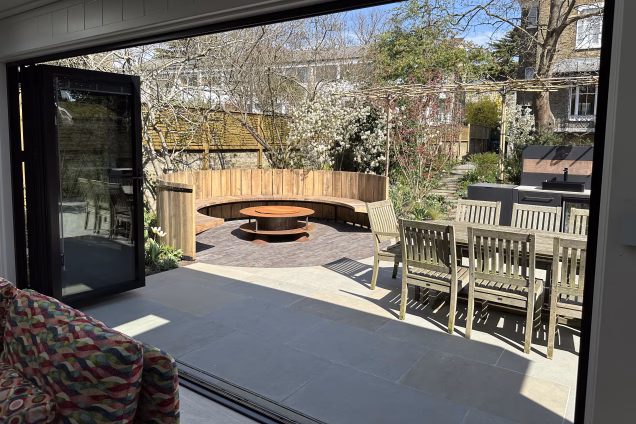 Photo looking out of a garden building in Blackheath London; the view is of a circular searing area and firepit in a landscaped garden