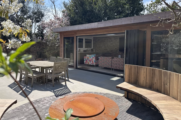 Portrait photo focused on a timber clad garden building with bifold doors by Bakers Garden Buildings