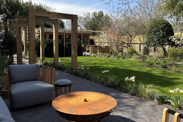 A stylish rusty firepit surrounded by comfortable all-weather outdoor armchairs in a landscaped garden in Blackheath, London