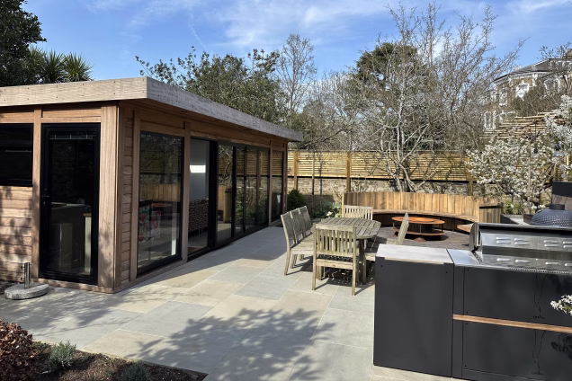 Outdoor living space in Blackheath London featuring table and chairs, garden building, outdoor kitchen and firepit