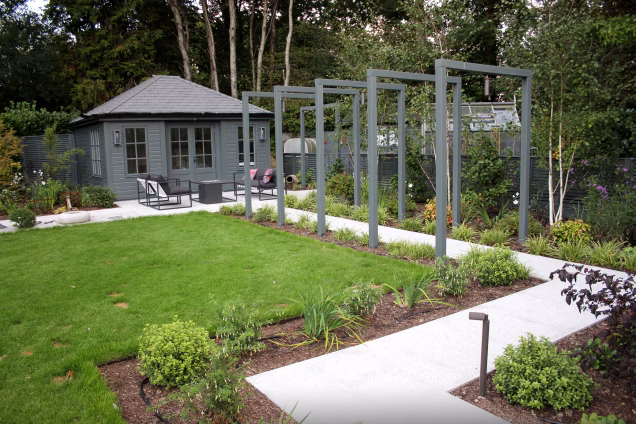 Grey arches along herbaceous bordered garden path leading to a summerhouse painted in the same shade of grey.