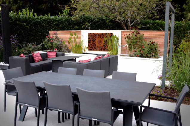 Outdoor seating and dining area in Cranleigh, Surrey, with an abstract art piece set behind wildflowers against a wall