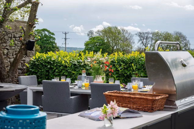 Gas grill in outdoor kitchen next to dining area in garden
