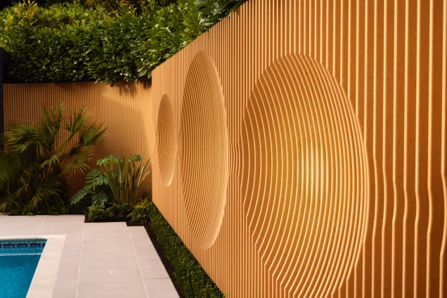 Profiled slatted garden walling arranged to form patterns, making a striking orangey backdrop to the swimming pool and garden