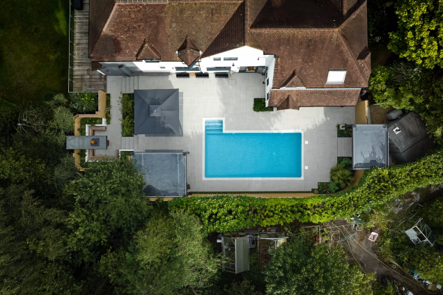 Vertical photo looking down on a side garden of a large house in Ashtead, Surrey. A blue swimming pool is centre frame