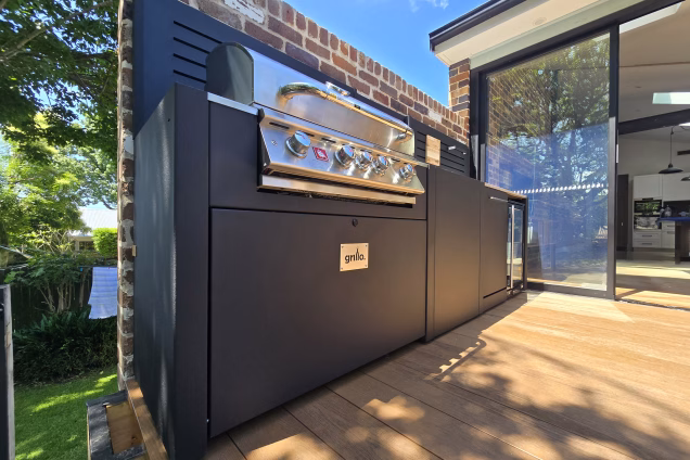 Low level photo looking along an outdoor kitchen into the open-plan kitchen-diner of a residential house in Naremburg NSW. The indoor living space leads seamlessly into the outdoor living space.