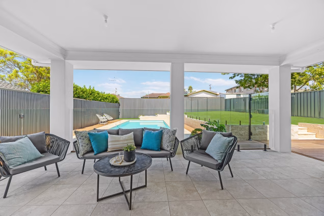 An alfresco area with comfy seating looking out across landscaped gardens and a swimming pool in Old Toongabbie