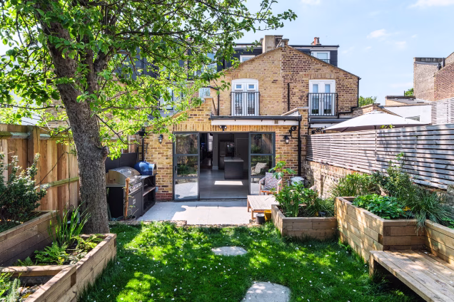 View looking towards the house in a back garden of a property in Stoke Newington. It's a sunny spring day and there is white blossom petals on the grass.