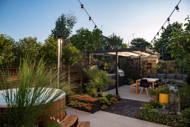 Looking across a Lewisham garden by Catherine Clancy Garden Designs, with a hot tub in the foreground and an outdoor kitchen dining area in the background