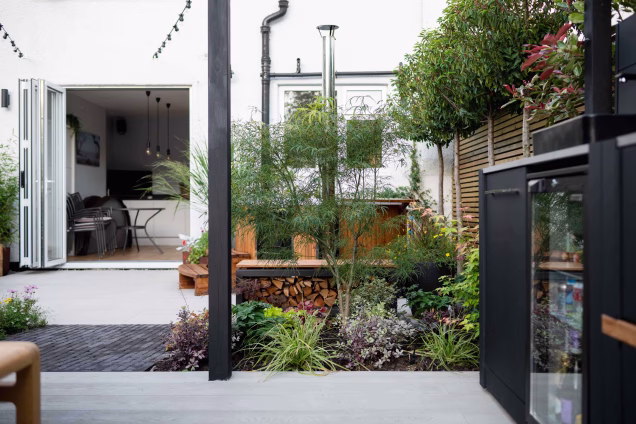 Looking towards the back of a house with landscaped garden, plantings, and an outdoor kitchen in the foreground