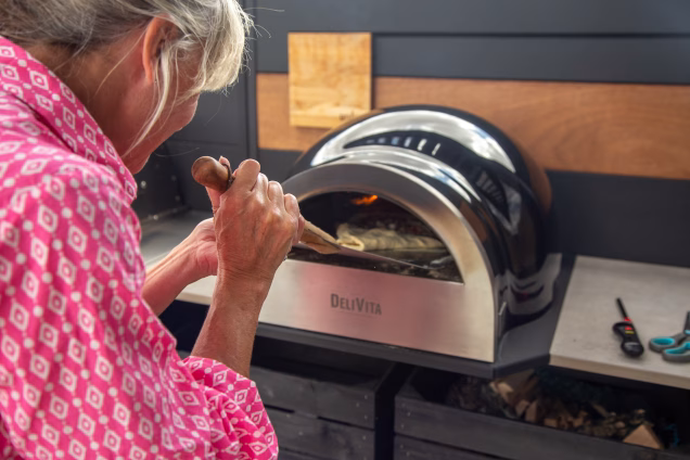 A closeup photo of Sara using a pizza peel to turn in pizza in a pizza oven