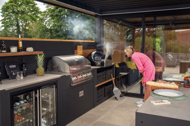 Sara cooks a pizza in a smoking pizza oven in her outdoor kitchen in Attleborough