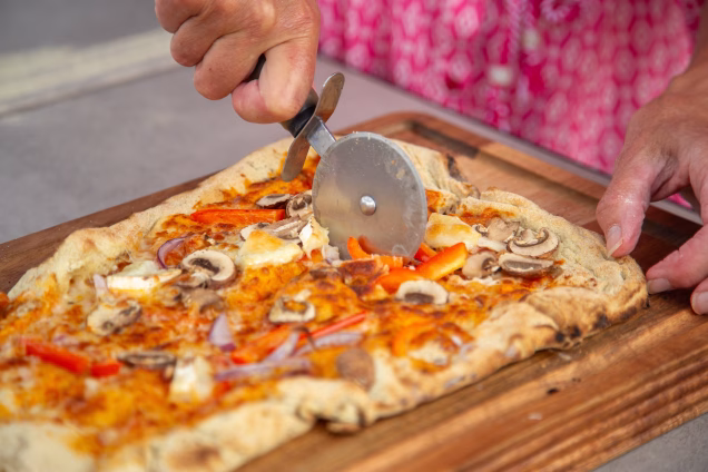 Closeup photo of a pizza wheel cutting a rectangular pizza in a Grillo outdoor kitchen