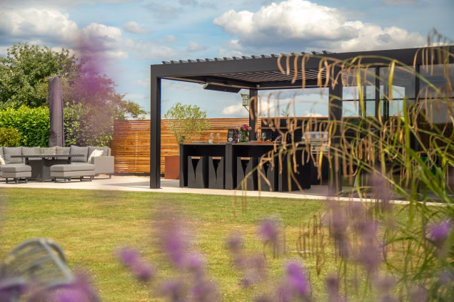 Looking towards a large semi-glazed pergola with a wrought iron garden bench and lavender out of focus in the foreground